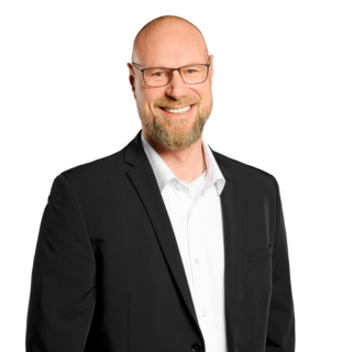 Porträt eines lächelnden Mannes im schwarzen Sakko vor hellem Hintergrund