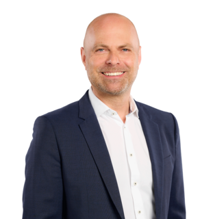 Porträt eines lächelnden Mannes im dunklen Anzug vor hellem Hintergrund